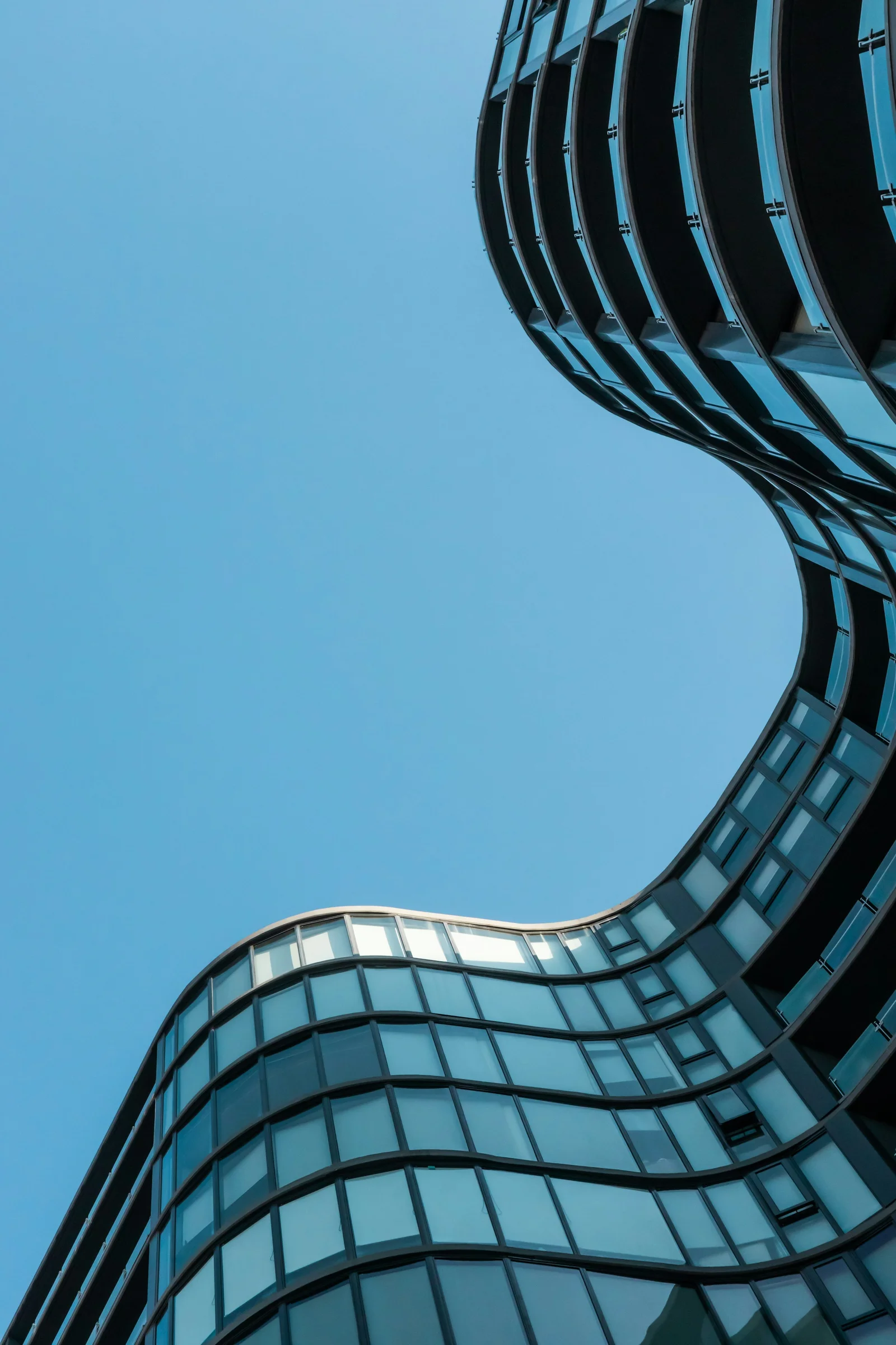Blaue Glasfassade mit geschwungenen Linien und weitem Blick in den Himmel